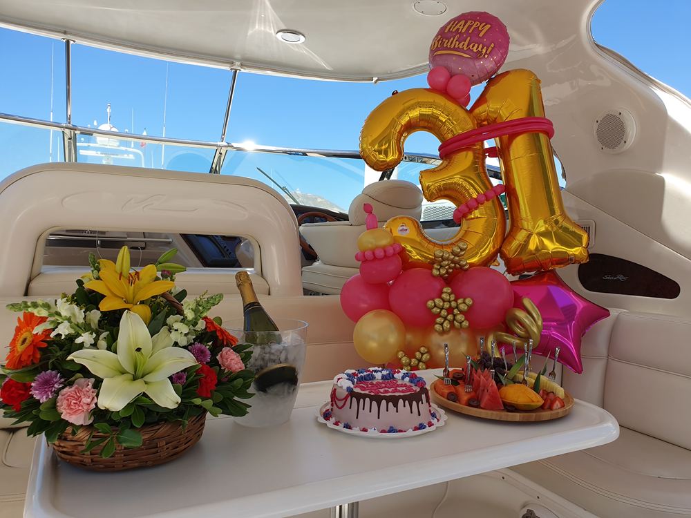 Gold number balloons, flowers and a cake set up for a birthday in a yacht's cockpit