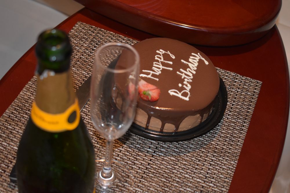 Happy Birthday chocolate cake beside a bottle of champagne and a glass on a yacht table