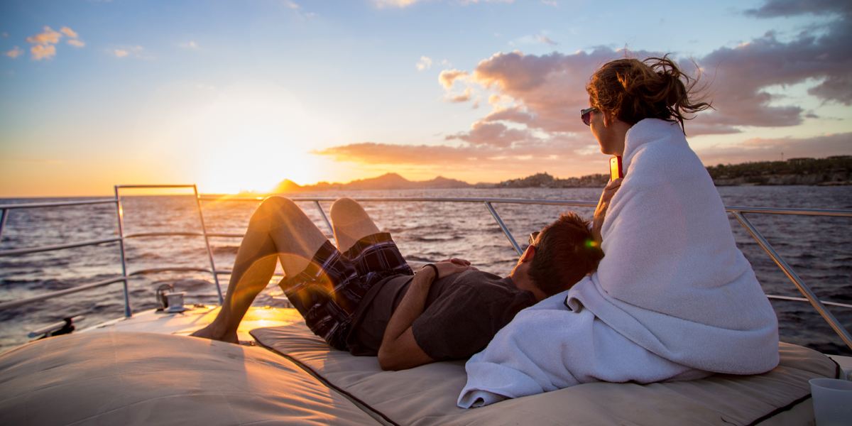 Couple relaxing on the bow of a yacht at sunset, wrapped in a white towel