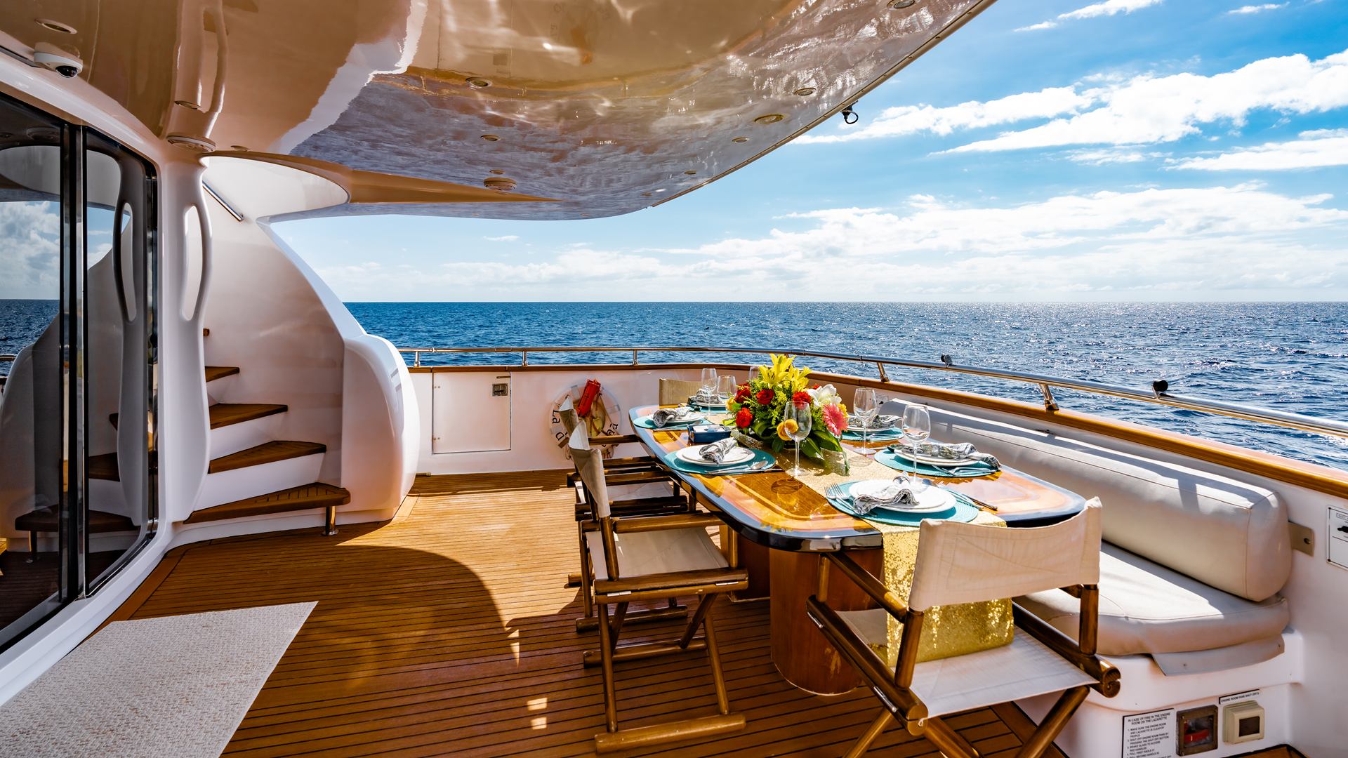 Aft deck of a motor yacht with a dining table set for lunch, flowers and an open sea view