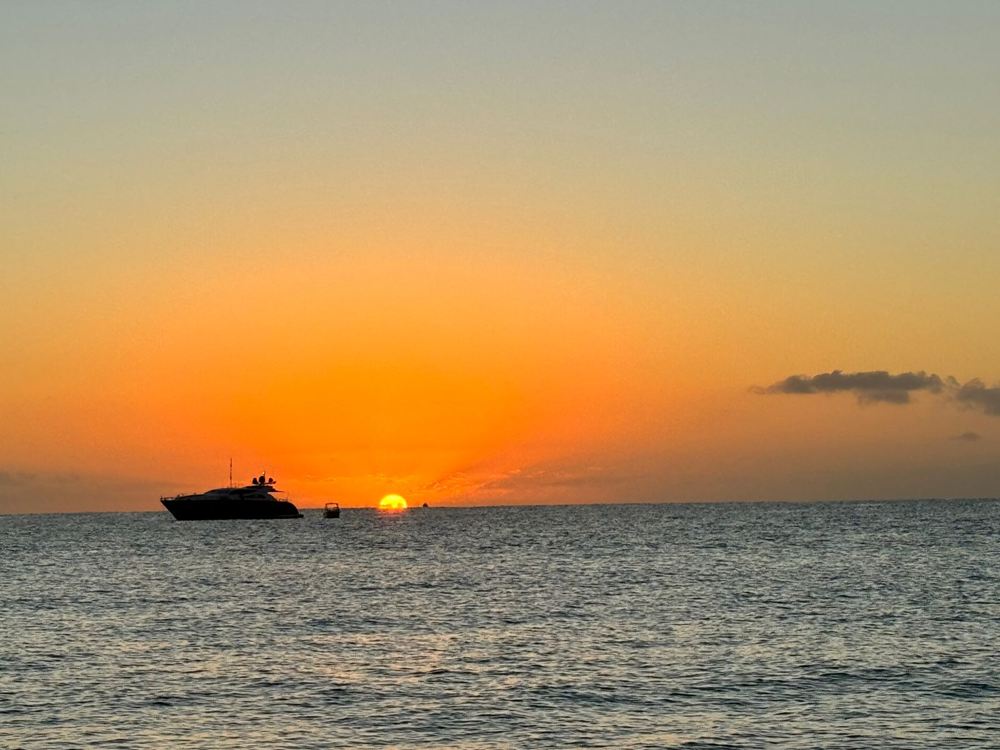 Motor yacht silhouetted against an orange sunset over a calm sea