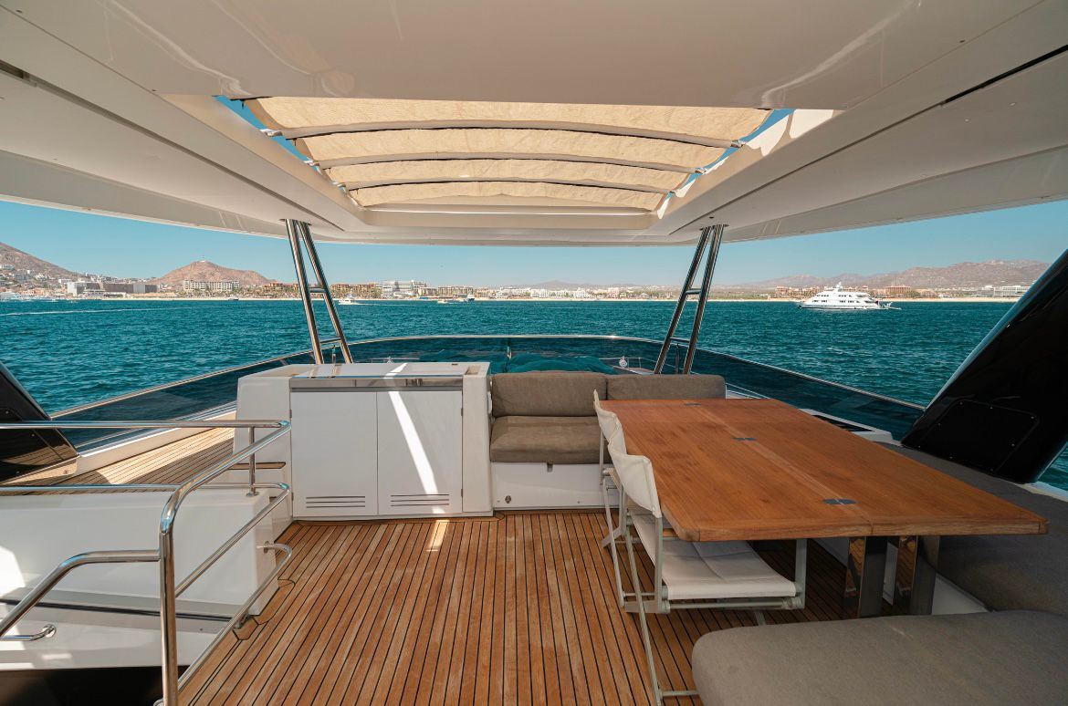 View from the shaded aft deck of a catamaran, with a dining table and the open sea beyond
