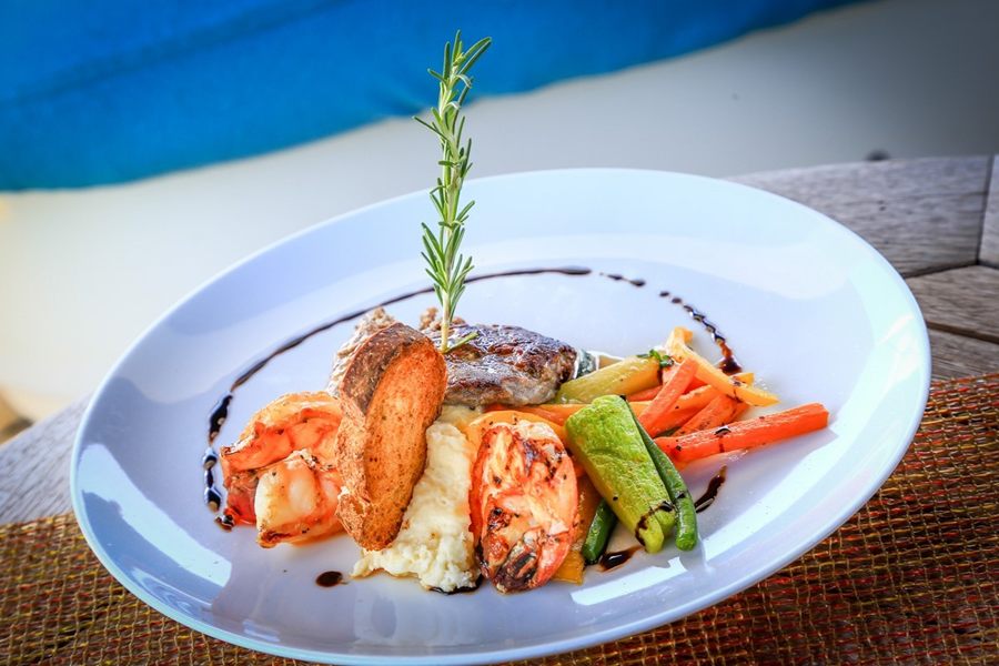 Plated seafood dish with vegetables and a rosemary garnish served on a yacht