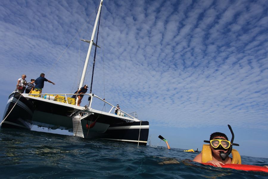 Snorkeler in a mask and life vest swimming beside a sailing catamaran