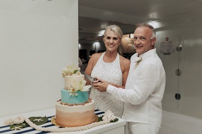 Bride and groom cutting a tiered wedding cake aboard a yacht
